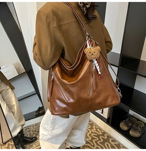 Detail view of large brown vintage tote bag with twin zippers and plush bear charm