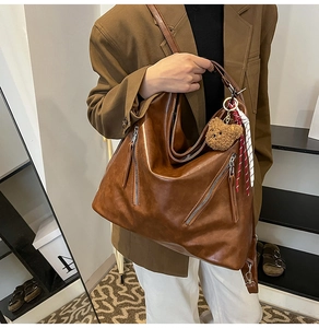 Close-up of vintage brown leather tote bag with decorative zippers and plush bear charm