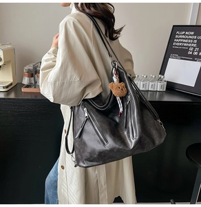 Détail d'un grand sac cabas en cuir noir texturé avec pendentif ours dans un café