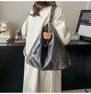 Detail view of large charcoal hobo bag featuring double zippers and a brown plush bear charm