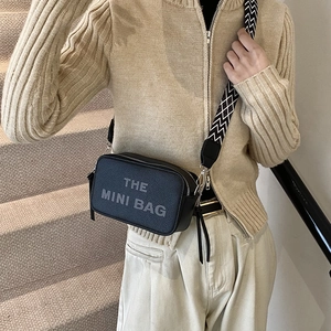 Stylish black leather mini crossbody bag with a wide geometric strap and text detail