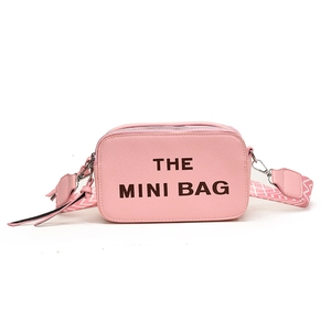 Pink mini crossbody bag with black THE MINI BAG text and geometric wide strap
