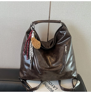 Détail du sac hobo en cuir marron foncé avec poches zippées et breloque ours en peluche