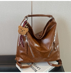 Détail d'un sac hobo en cuir marron avec zips et breloque d'ours en peluche doux