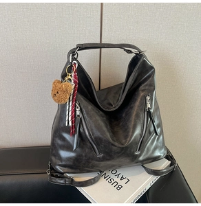 Detail of black faux leather tote with silver zippers and a cute brown bear charm
