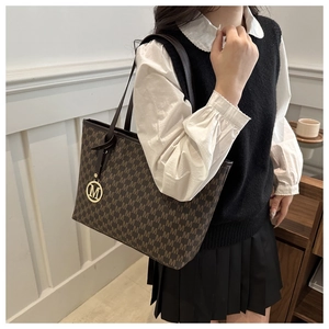 Detail view of brown tote bag with M-letter jacquard pattern and golden metallic charm
