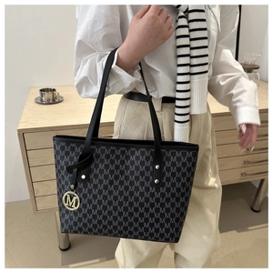 Detail of black leather tote bag with gray M letter print and gold logo pendant
