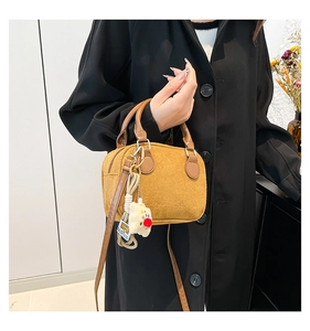 Detail of yellow suede pillow bag with brown leather handles and a plush bear charm