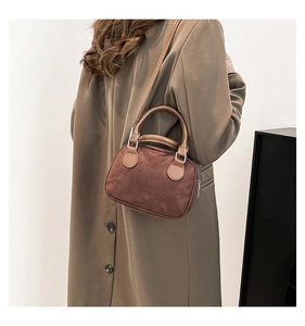 Detail of brown suede bowling bag with smooth leather handles worn with a long coat