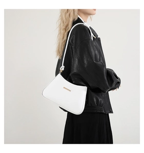 Close-up of elegant white leather shoulder bag with gold hardware worn with a black jacket