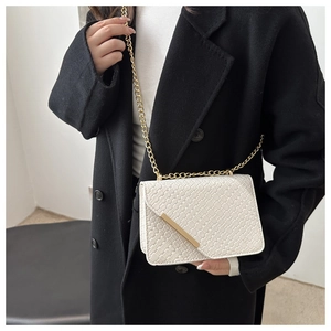 Close-up of white woven leather crossbody bag with gold hardware on a black coat