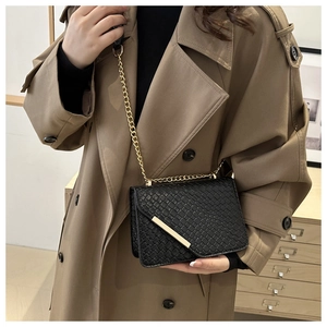 Detail of black woven crossbody bag with gold chain worn over a khaki trench coat