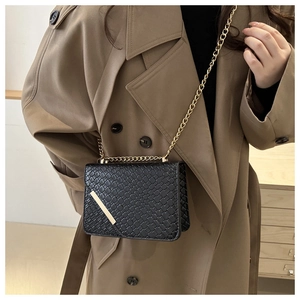 Detailed view of black woven texture crossbody bag with gold chain on camel coat