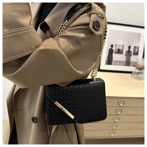 Detail of black crossbody bag with snake texture and gold chain on model