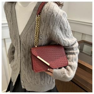 Detail of red crocodile texture crossbody bag with gold chain strap on a model