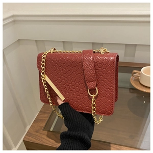 Detail of dark red woven texture bag with gold chain strap held by model in home setting