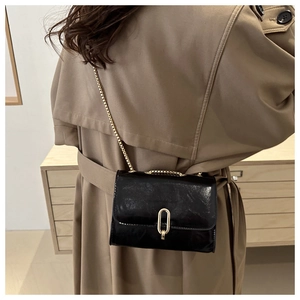 Detail of black glossy crossbody bag with gold ring buckle worn by a model in a trench coat