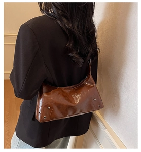 Brown leather shoulder bag with metallic rivets shown on a model for size scale