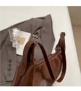 Detail view of smooth adjustable leather shoulder strap and metallic buckle on brown tote