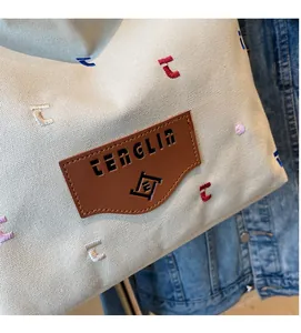 Close-up of beige canvas tote with colorful letter embroidery and brown leather patch