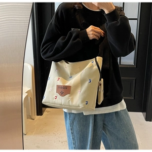 Detail of canvas tote bag with letter embroidery and a side hanging zipper pouch