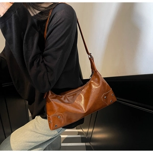 Dettaglio di una borsa a spalla in pelle marrone lucida con borchie argentate sul lato