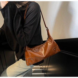 Close-up of brown glossy shoulder bag with white contrast stitching and silver studs