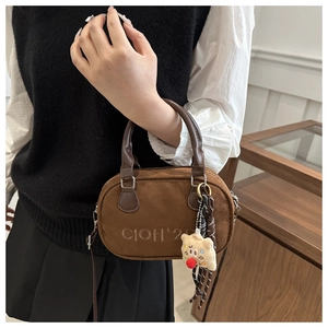 Details einer dunkelbraunen Wildlederhandtasche mit Logo-Prägung und Bären-Anhänger