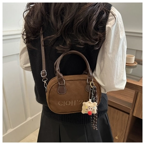 Detail of dark brown suede handbag with plush charm and embroidery on back of model
