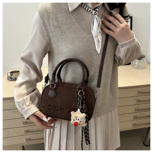 Detail view of coffee suede bag featuring embroidery and plush doll charm hanging from strap