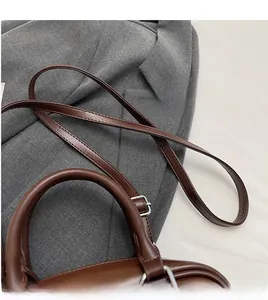 Détail d'un sac à main en cuir marron avec poignée renforcée et bandoulière argentée réglable
