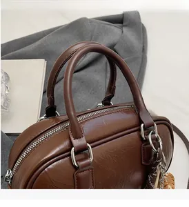Détail du sac Boston en cuir gaufré marron foncé avec doubles anses et zip argenté