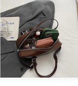 Vue détaillée de l'intérieur spacieux du sac Boston marron contenant téléphone et parfum