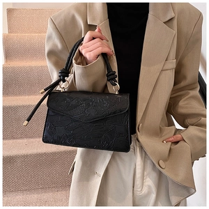 Detail of black leather handbag with embossed lotus koi patterns and golden metal ring handle
