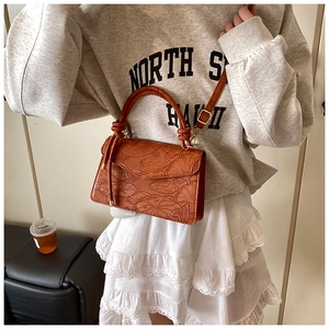 Detail of caramel embossed leather handbag featuring vintage lotus patterns and metal buckle