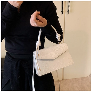 Detail of white handbag with floral embossing, knotted handle and gold metal ring