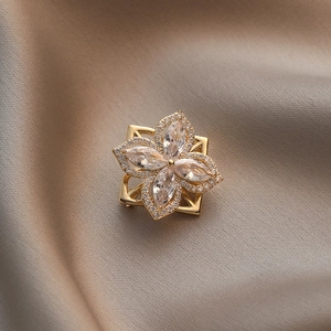 Eleganter goldener Blumenanstecker mit Zirkonia-Steinen auf glänzendem Seidenstoff