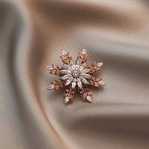 Elegant snowflake brooch with amber and white crystals on a champagne silk background