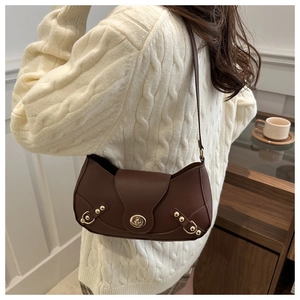 Close-up of retro brown leather saddle bag with gold clasp worn over a beige sweater