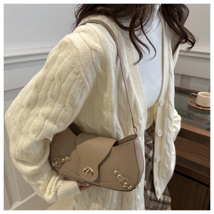 Detail view of a vintage khaki underarm bag with gold rivets on a knitted cardigan
