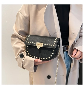 Detail of black pebbled leather crossbody bag with gold rivets and chain strap on model