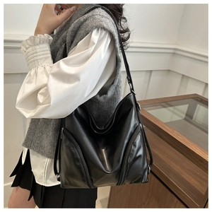 Detail view of large black shiny PU leather backpack with side zippers on a female model
