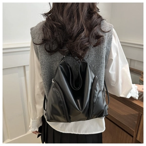 Detail of a soft black leather backpack showing vertical metal zippers and its sleek texture