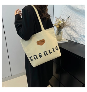 Detail of minimalist beige canvas tote bag with brown leather brand tag and letter print