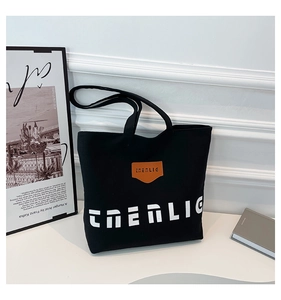 Detailed view of black canvas tote bag featuring orange logo patch and white typography