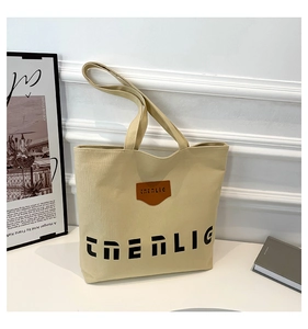 Close-up of beige canvas tote with large black lettering and a brown leather logo patch