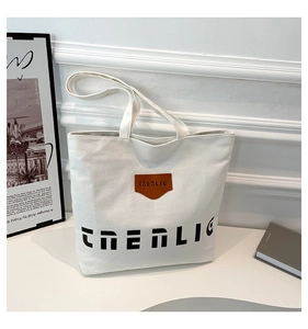 Close-up of a white canvas tote bag featuring THENLIG text and a brown leather logo tag