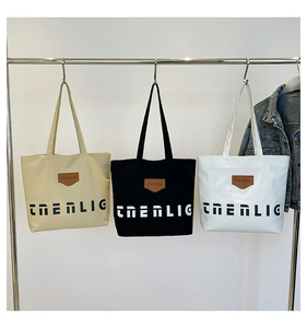 Three canvas tote bags in beige, black and white colors hanging on a minimalist metal rack