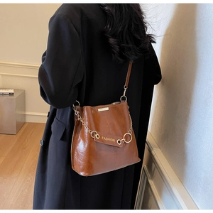 Brown glossy leather shoulder bag with gold chain and fashion tag on model back