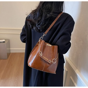 Detail of a brown glossy bucket bag with golden chain and adjustable strap on a model